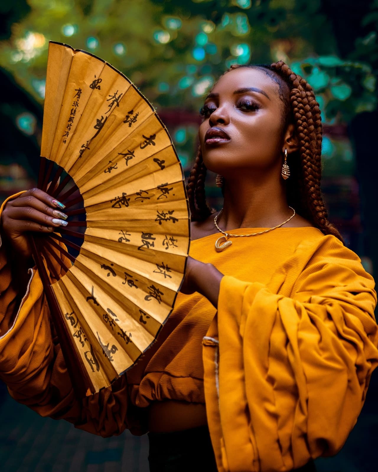 A woman with long braids holding a yellow fan